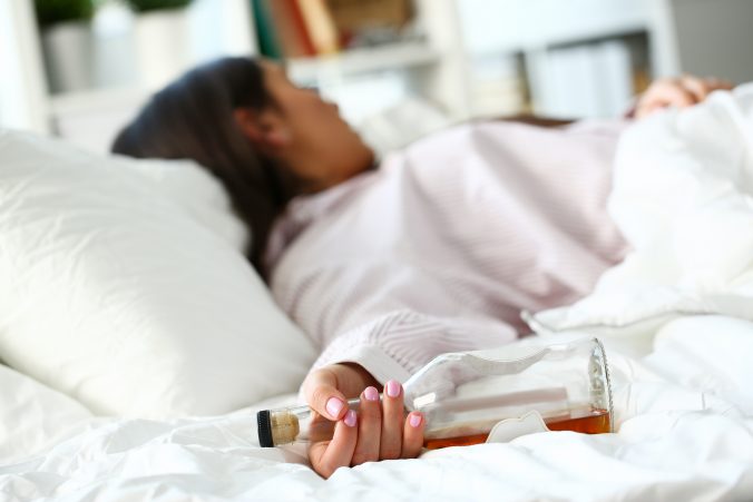 Frau mit Flasche liegt im Bett. Es sieht aus als ob sie einen Rückfall hat Foto von Adobe Stock